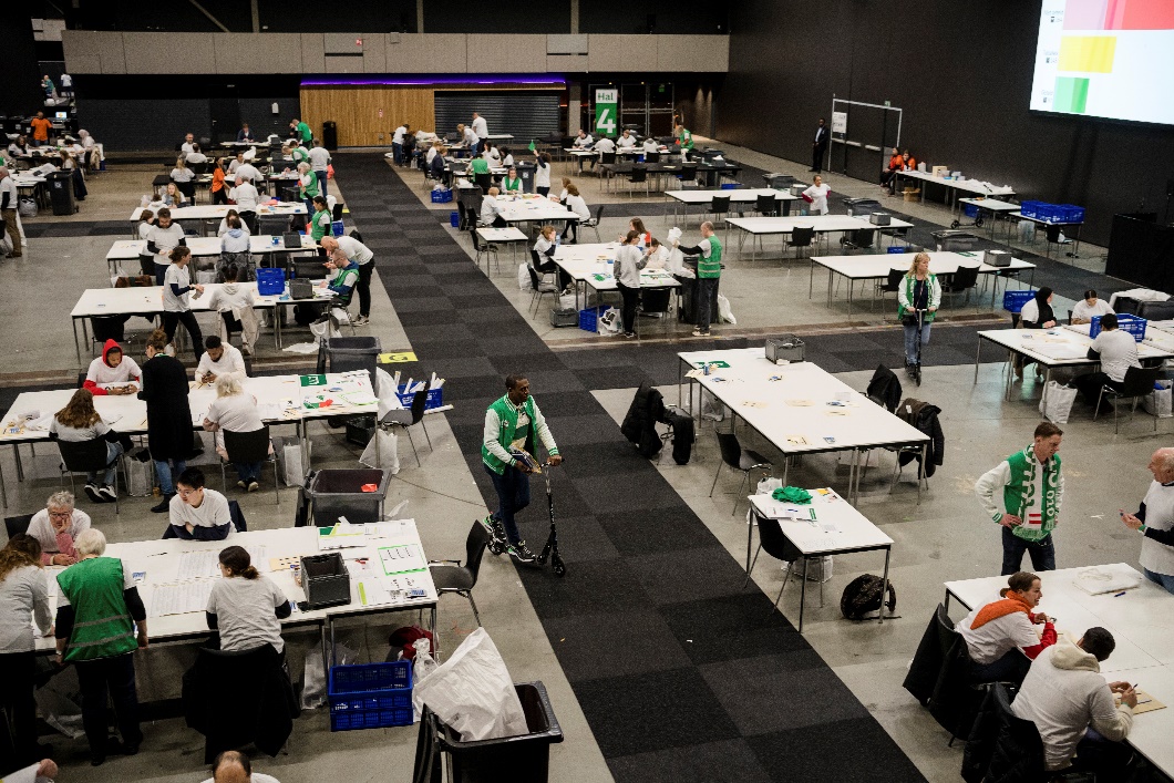a sports hall with tables where people are counting ballots